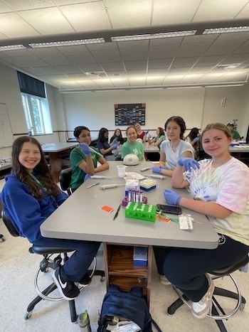 A group of students sitting at a table in the lab smiling at the camera.